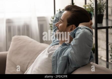 Happy millennial man sit on sofa hold hands behind head Stock Photo