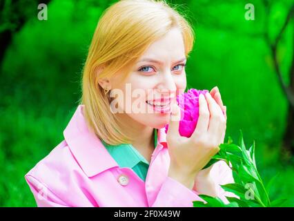 Cute woman smelling Peony flower. Beautiful girl with pink flower. Romantic female in spring park. Stock Photo