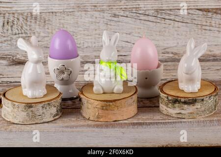 Easter rabbits and candles in the shape of Easter eggs on a wooden table. Stock Photo