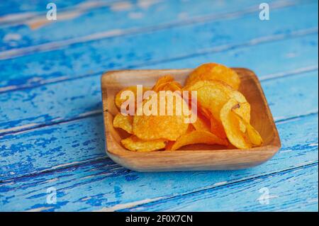 potato chips in a wooden bowl on blue background with copy space Stock Photo