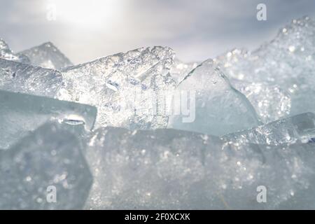 Transparent shining clear ice icicles close-up sparkling on frozen wild lake shore in sunset light. Cold winter nature background Stock Photo