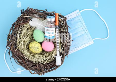 Vaccine vial, syringe, surgical mask and easter egg nest flatlay Stock Photo