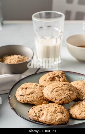 Close up front view on crunchy oatmeal chip cookies fresh baked biscuits with chocolate and cocoa in a plate on the table and ingredients beside homem Stock Photo