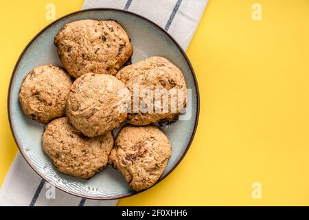 Close up top view on crunchy oatmeal chip cookies fresh baked biscuits with chocolate and cocoa in a plate on the yellow modern abstract background - Stock Photo