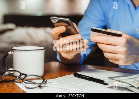 Stressed young businessman calculating monthly Family expenses, taxes, checking bank account balance credit card payment, Income at home night. Croppe Stock Photo