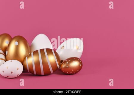 Group of golden and white Easter eggs painted with simple dots and stripes on side of pink background Stock Photo