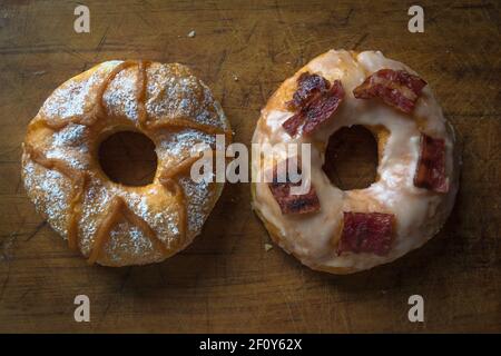 Two delicious desserts one white glazed bacon donut or doughnut and seet milk and suger on a wooden board Stock Photo