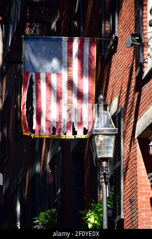 Betsy Ross flag hangs over the colonial house fronts along Acorn St. in Boston with brick and streelight features. Stock Photo