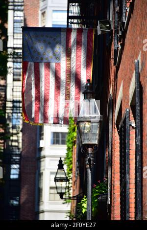 Betsy Ross flag hangs over the colonial house fronts along Acorn St. in Boston with brick and streelight features. Stock Photo