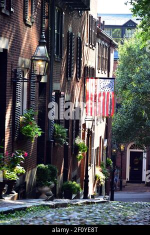 Betsy Ross flag hangs over the colonial house fronts along Acorn St. in Boston with brick and streelight features. Stock Photo