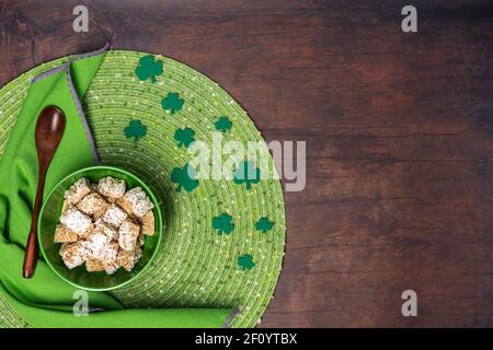 St Patricks day breakfast of frosted wheat cereal in a green bowl with a placemat, napkin and wooden spoon on a wood table background Stock Photo
