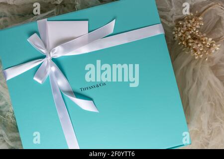Flourtown, PA - Feb. 22, 2021: Tiffany gift box with white satin ribbon and gift card on a background of soft focus faded antique wedding veil with pe Stock Photo