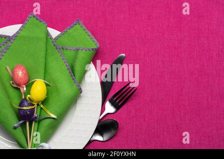 bright Easter or springtime place setting of a white basketweave pattern plate with green napkin and egg decor on a pink tablecloth Stock Photo