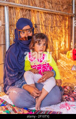 Middle East, Arabian Peninsula, Oman, Ash Sharqiyah North, Bidiya. Oct. 26, 2019. Omani woman in blue hijab and metallic battoulah with a young girl. Stock Photo