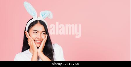 Happy Easter Day. Beautiful young woman teen smiling wearing Easter rabbit bunny ears holding her cheeks excited surprised, Portrait female face touch Stock Photo