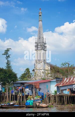 Boat and riverside housing on the Mekong river, Cai Be, Tien Giang Province, Mekong Delta , Vietnam. The Catholic cathedral, Cai Be Stock Photo