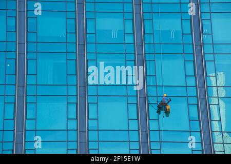 Absailing window cleaner cleaning windows on a blue glass skyscraper, Ho Chi Minh City, Vietnam. Stock Photo