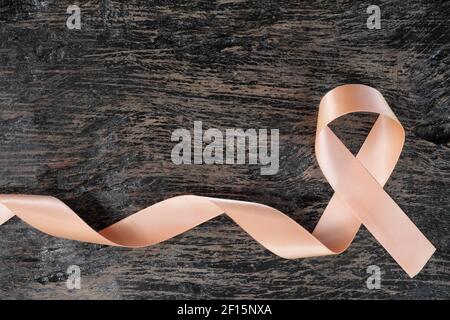 Top view of peach ribbon on dark wood background. Uterine and endometrial cancer awareness concept. Stock Photo