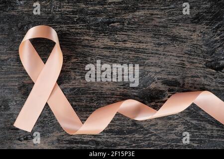 Top view of peach ribbon on dark wood background. Uterine and endometrial cancer awareness concept. Stock Photo