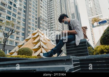 Young asian man with protective mask is sitting outside writing on leather notebook during an epidemic. Healthcare and education concept. Stock Photo