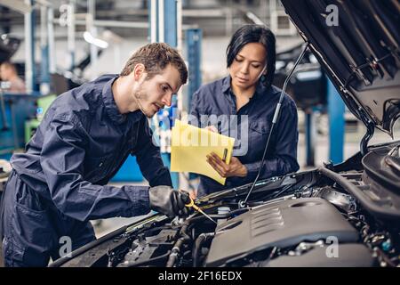 Auto car repair service center. Two mechanics - man and woman examining car engine Stock Photo