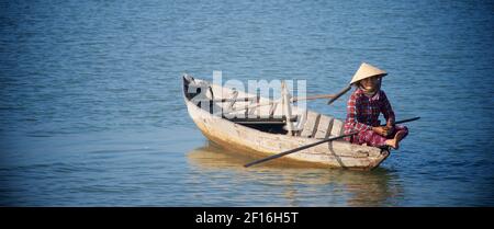 Vietnamese woman in distinctive conical hat in a small boat on the Thu Bon river, Hoi An, Vietnam. Stock Photo