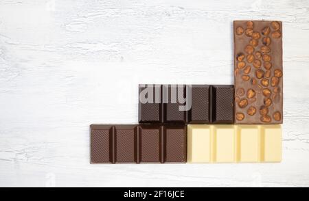 a lot of different sweet, delicate chocolate bars lie creatively on a white wooden background Stock Photo