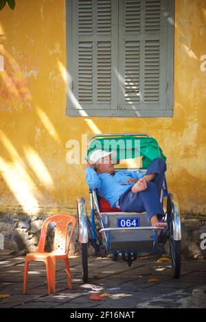 Vietnamese rickshaw driver resting in his rickshaw. Hoi An, Vietnam Stock Photo