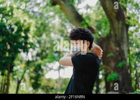 Asian man wear mask that protect against covid 19 warming up for health in the park.Social distancing, work out and new normal concept. Stock Photo