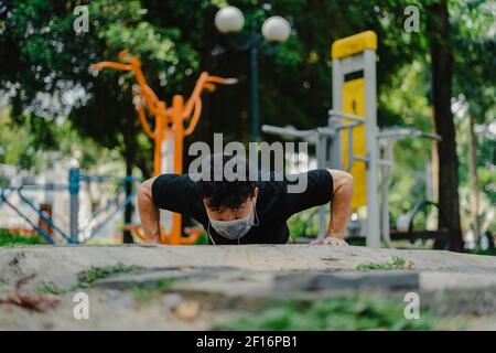 Asian man wear mask that protect against covid 19, doing press ups in park for health in the park. Social distancing, work out and new normal concept. Stock Photo