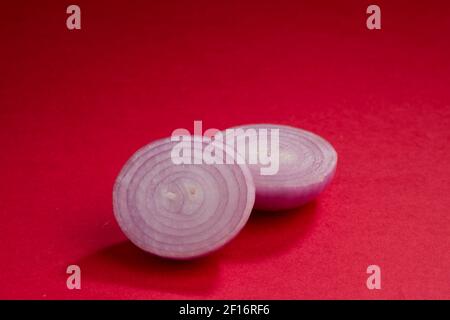 Onion slices, arranged beautifully on a red textured background, isolated. Stock Photo