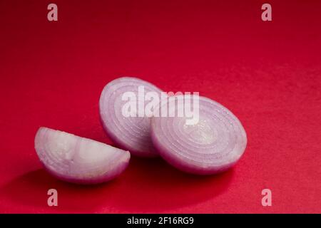 Onion slices, arranged beautifully on a red textured background, isolated. Stock Photo