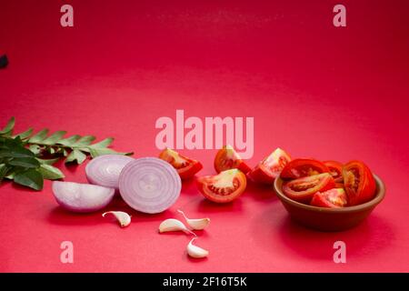 Tomato ,curry leaves,garlic cloves and onion slices arranged in an earthen ware with reddish background Stock Photo