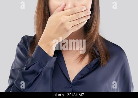 The woman in a dark blue shirt not commenting and refusing. woman with her hands on her mouth because of bad breath or halitosis Stock Photo