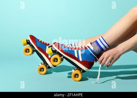 Young woman tying the laces on her red and blue rollerskates with colorful yellow wheels in a close up side view of her feet and hands over a blue bac Stock Photo