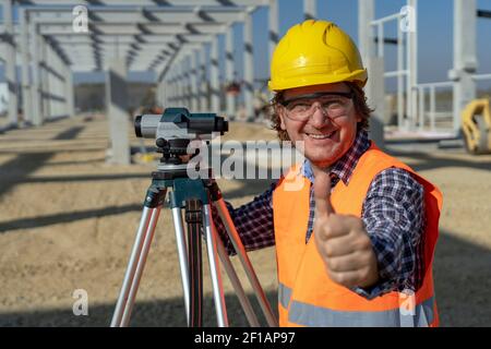 Smiling Construction Worker With Measuring Device Giving Thumb Up at a Construction Site. Stock Photo