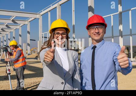 Smiling Female Architect and Mature Businessman With Thumbs Up at a Construction Site. Business Success, Relationship and Teamwork Concept. Stock Photo