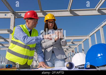 Mature Businessman and Female Architect on Building Site Checking Blueprint. Business Relationship and Teamwork Concept. Stock Photo