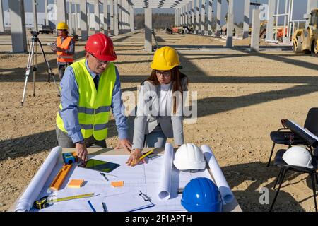 Mature Businessman and Young Female Architect Planning Construction Project at Construction Site. Business Relationship and Teamwork Concept. Stock Photo