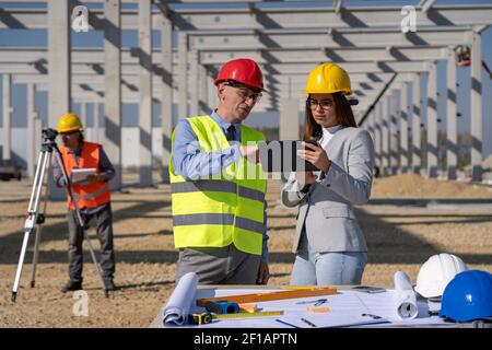 Young Female Architect With Tablet and Mature Businessman Meeting on Construction Site. Business Relationship and Teamwork Concept. Stock Photo