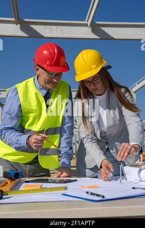 Smiling Mature Businessman and Young Female Architect Planning Construction Project at Construction Site. Business Relationship and Teamwork Concept. Stock Photo