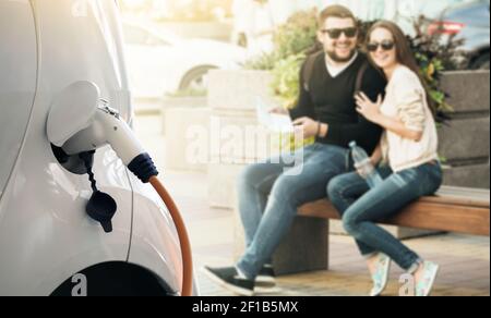 Close up of charging electric car. Smiling couple on a background  Stock Photo