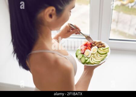Young brunette fitness woman athete in sportswear standing and eating healthy meal Stock Photo