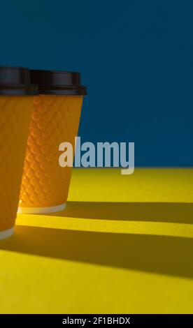 Yellow ribbed paper cup with plastic lid for takeaway beverage in fast food restaurants. A cup of coffee, cocoa, tea from a street cafe. Place for your text. Blue background. Stock Photo