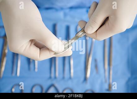 Close up view of doctor's hands holding scalpel for plastic surgery. Surgeon with stainless steel medical instrument in arms wearing white sterile gloves. Concept of surgery and medicine.