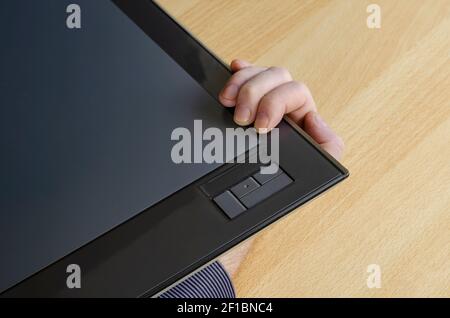 Designer's hand holding a graphic tablet from below. A man's hand and a professional device for designers. Digital technology. View from above at an a Stock Photo