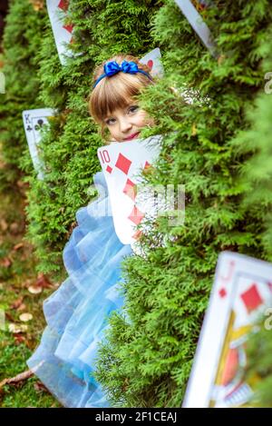 An little beautiful girl in a long blue dress looking from under the fir trees Stock Photo