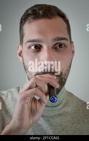 Portrait of a young bearded man who smokes an electronic cigarette, close up Stock Photo