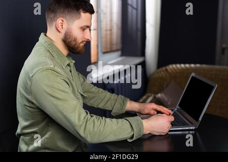 Brunette, young and handsome businessman, programmer working with laptop at home or in a business office. The concept of focusing on the success of Stock Photo