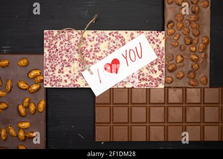 different sweet bars of chocolate lie on a black wooden background with a label that says I love you Stock Photo